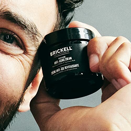 Man holding Brickell anti-aging cream close to his face.